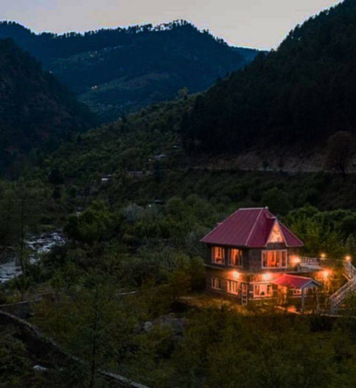 Kathkuni villa glowing at dusk beneath forested mountains