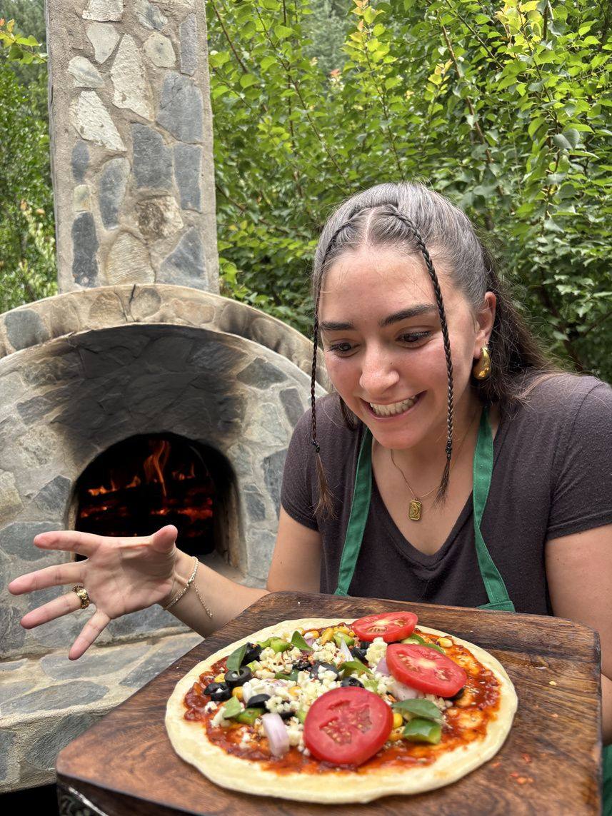 Guest pulling a wood-fired pizza from the clay oven
